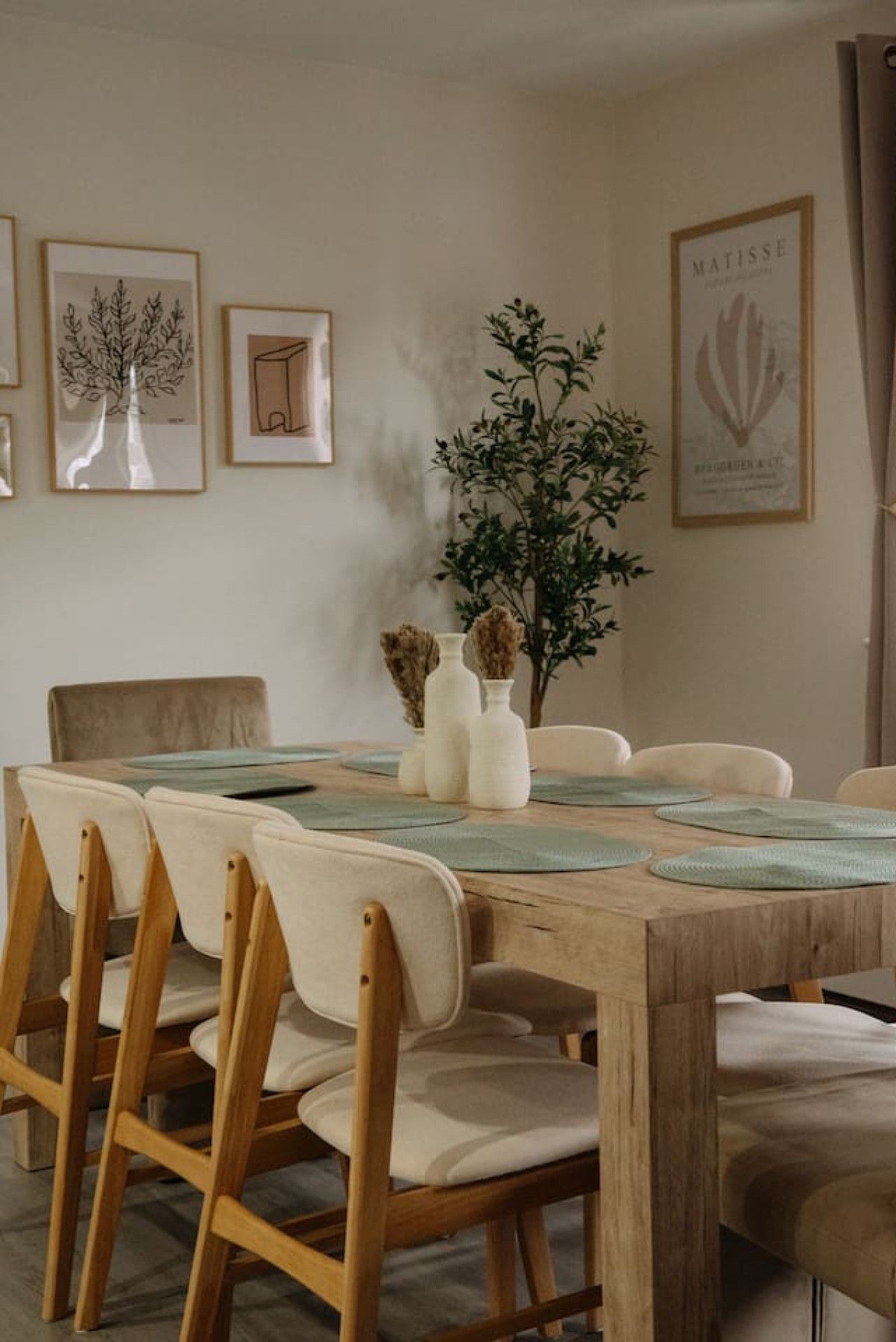 Un comedor con una mesa de madera, sillas blancas y obras enmarcadas en las paredes.