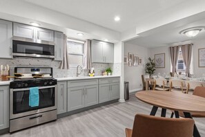 Cozinha moderna com armários cinza, fogão de aço inoxidável e área de jantar com mesa e cadeiras de madeira.