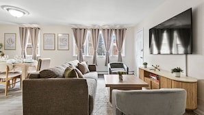 A modern living room with a sofa, armchairs, a dining table, and a TV mounted on the wall. - Big City Retreat with Parking (North Bergen)