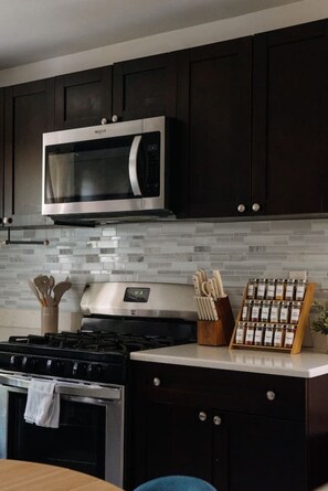 A kitchen with dark cabinets, a stainless steel microwave, a gas stove, and a spice rack. - NEW Spacious Chic Escape min NYC w/Parking (North Bergen)