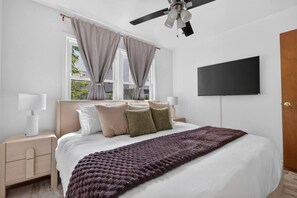 Ein Schlafzimmer mit einem Bett, Nachttischen, einem Fernseher und einem Deckenventilator.