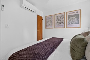 A bedroom with a bed, a wooden door, and three framed artworks on the wall. - NEW Spacious Chic Escape min NYC w/Parking (North Bergen)
