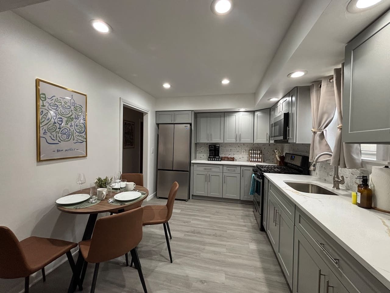 A modern kitchen with grey cabinets, a stainless steel refrigerator, and a dining area with a table set for two.