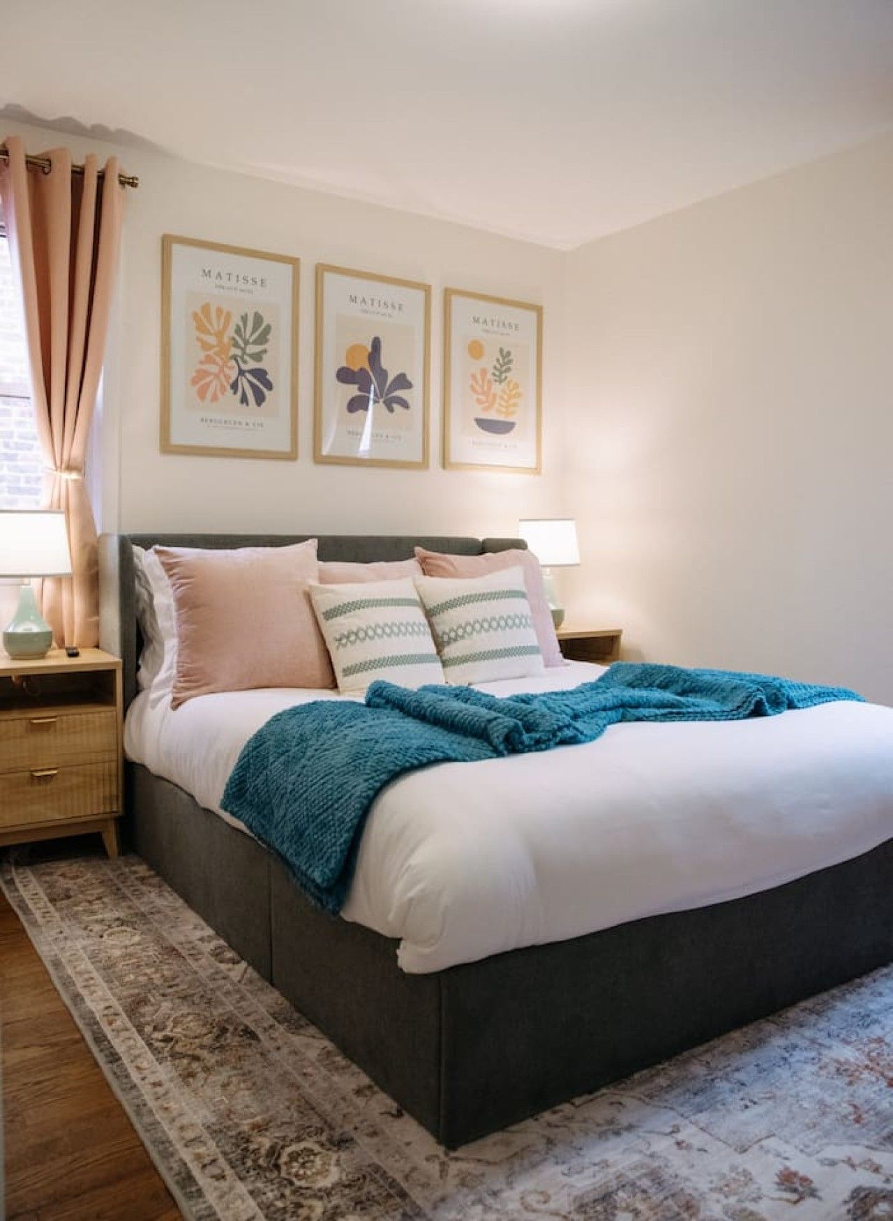 A bedroom with a bed, nightstands, a rug, and three framed artworks on the wall.