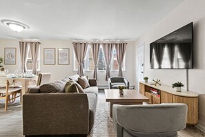 Una sala de estar moderna con un sofá, sillones, una mesa de comedor y un televisor montado en la pared.