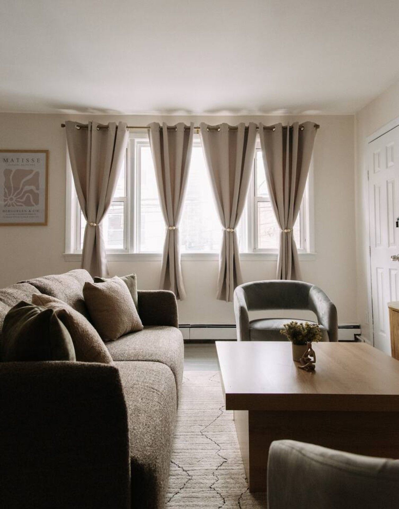Una habitación con sofá, una silla, una mesa y un ventanal con cortinas.