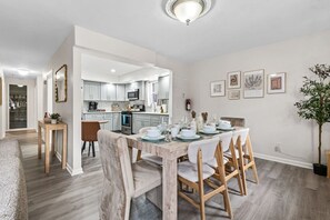 Una cocina moderna con armarios blancos, un comedor con mesa y sillas de madera, y una sala de estar con sofá y mesa de centro.