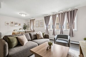 Una sala de estar moderna con un sofá, una silla, una mesita de centro y un comedor con una mesa dispuesta para dos personas.