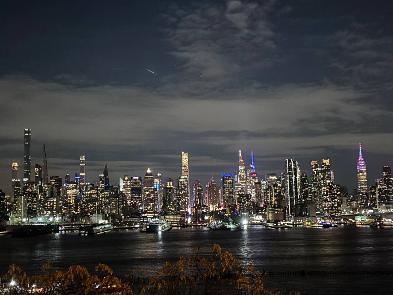 A nighttime city skyline with illuminated buildings and a body of water in the foreground.