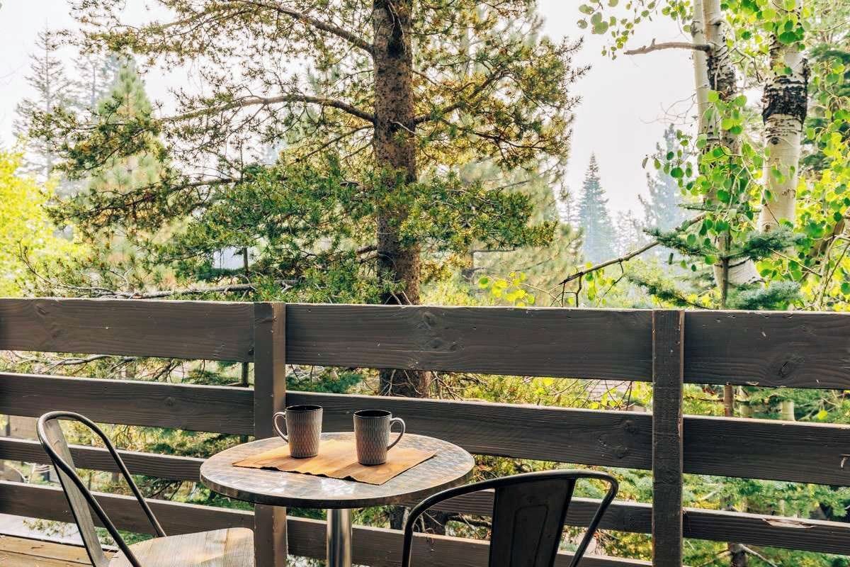 A wooden deck with a round table and two chairs, surrounded by trees.