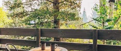 A wooden deck with a round table and two chairs, surrounded by trees.