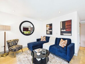 A modern living room with a blue sofa set, a round mirror, and a coffee table. - Westminster Duplex 2BR Apartment with Balcony (Greater London)
