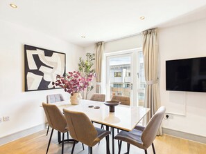 Et moderne spiseområde med et bord, stole, en vase med blomster og et stort vindue med gardiner.