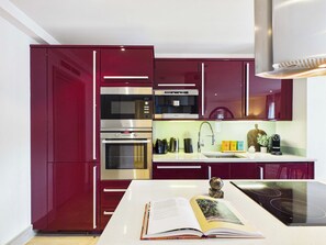 Una cocina moderna con electrodomésticos de acero inoxidable, una encimera blanca y armarios rojos.