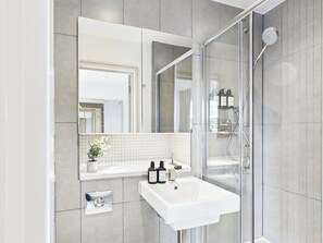 Ein modernes Badezimmer mit einer Glaskabine zur Dusche, einem weißen Waschbecken und einem Spiegel darüber.