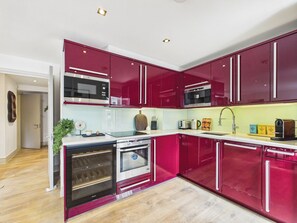 A modern kitchen with red cabinetry, stainless steel appliances, and a wooden floor. - Spacious Westminster Duplex Apartment with Balcony (Greater London)
