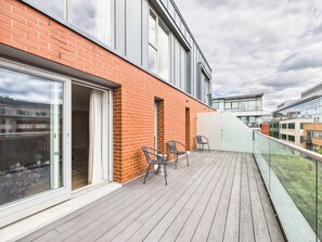 Ein Balkon mit Holzboden, zwei Stühlen und einer Glastür zu einem Innenbereich.