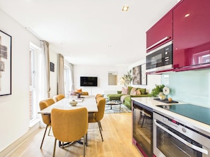 Eine moderne Küche mit Einbauofen und Mikrowelle, ein Essbereich mit Tisch und Stühlen sowie ein Wohnbereich mit Sofa und Fernseher.