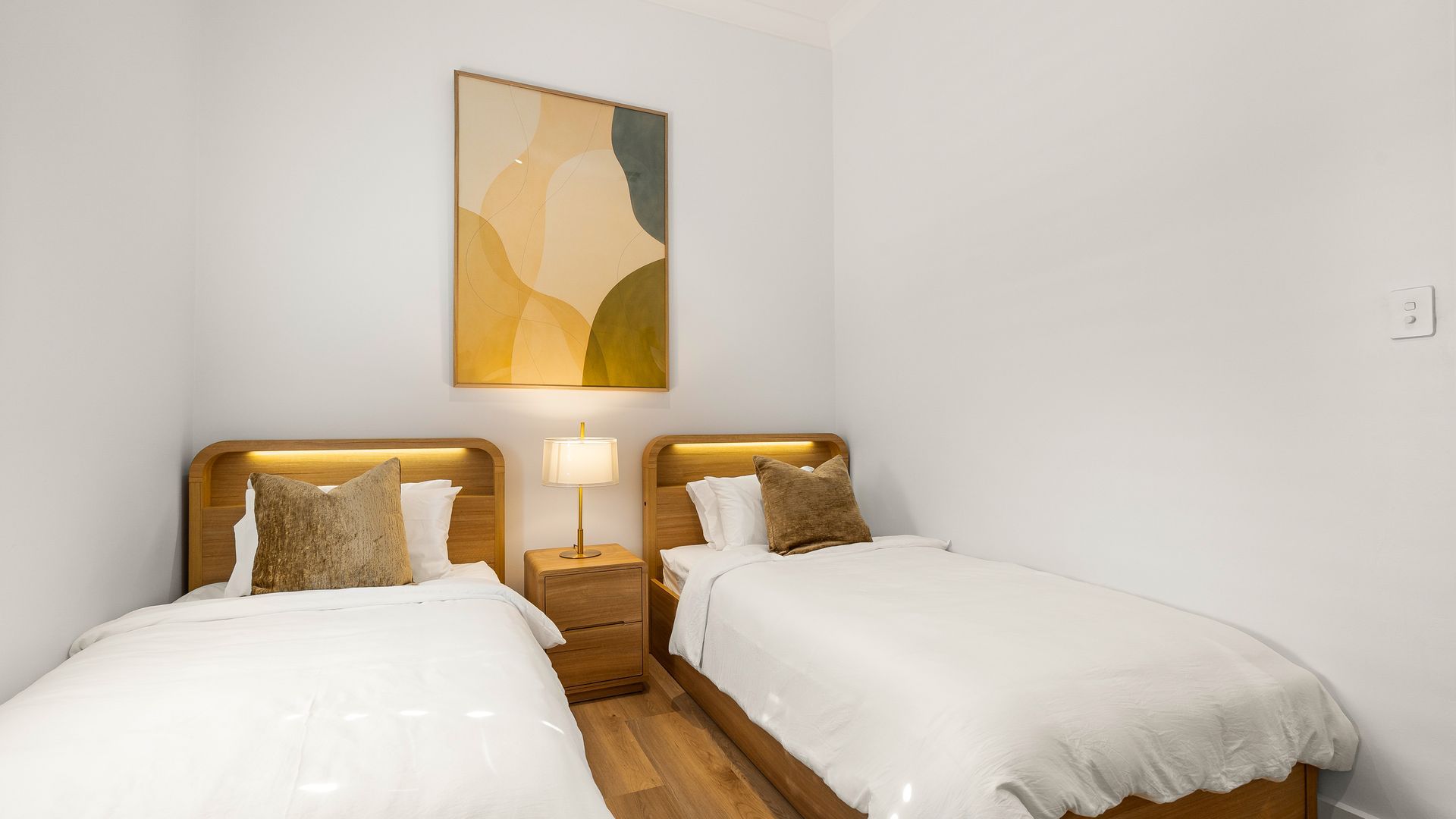 Ein Hotelzimmer mit zwei Betten, einem Nachttisch, einer Lampe und einem an der Wand hängenden abstrakten Gemälde.