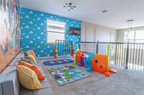 Zona de juegos infantiles con una pared colorida, una ventana, un sofá y un parque infantil.