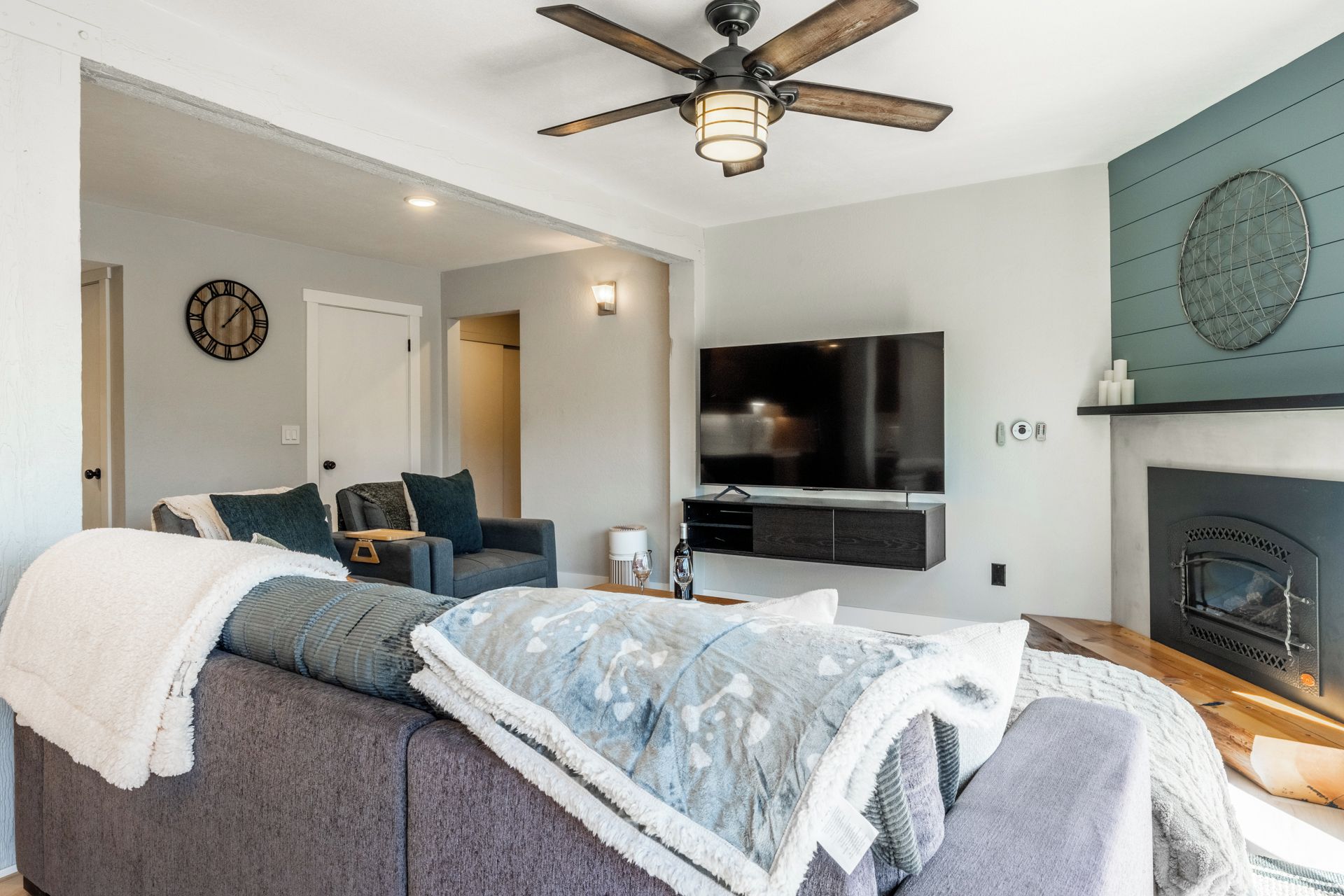 Ein modernes Wohnzimmer mit Sofa, Fernseher, Kamin und Deckenventilator.