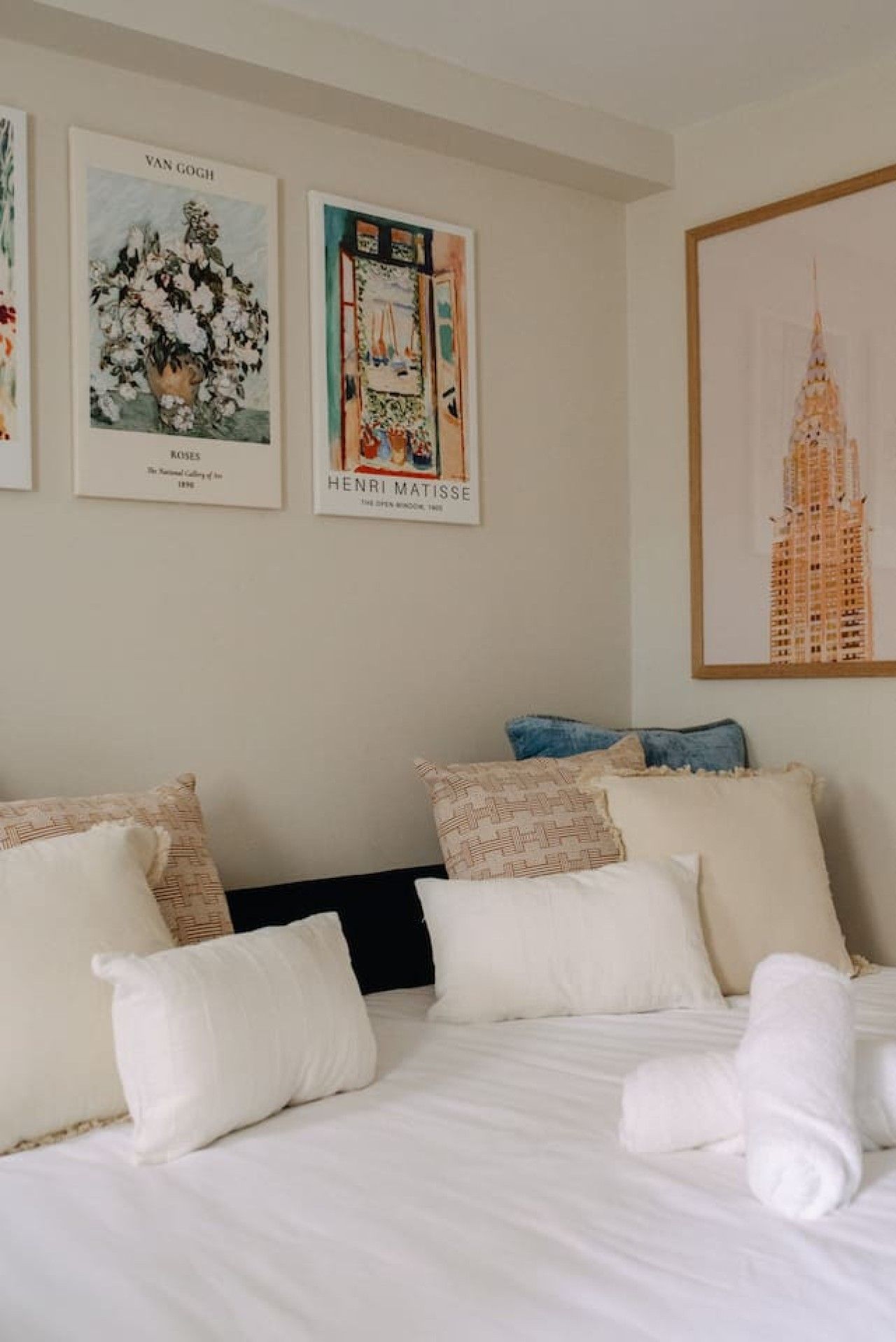 A hotel room with a bed, pillows, and three framed artworks on the wall.