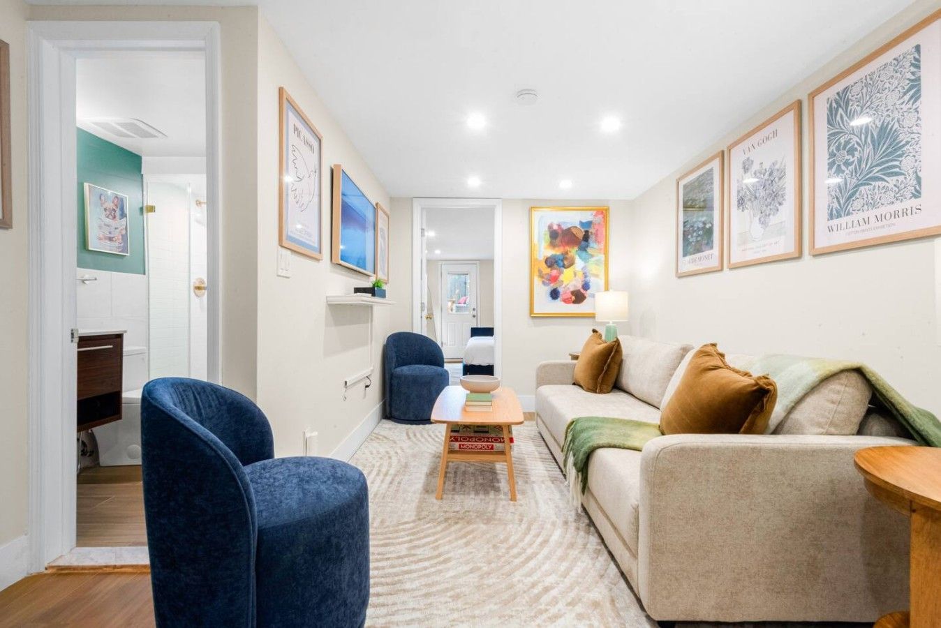 A living room with a sofa, armchairs, a coffee table, and a TV. There are framed artworks on the walls.