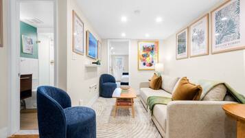 A living room with a sofa, armchairs, a coffee table, and a TV. There are framed artworks on the walls.