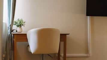 A room with a desk, chair, and a potted plant.