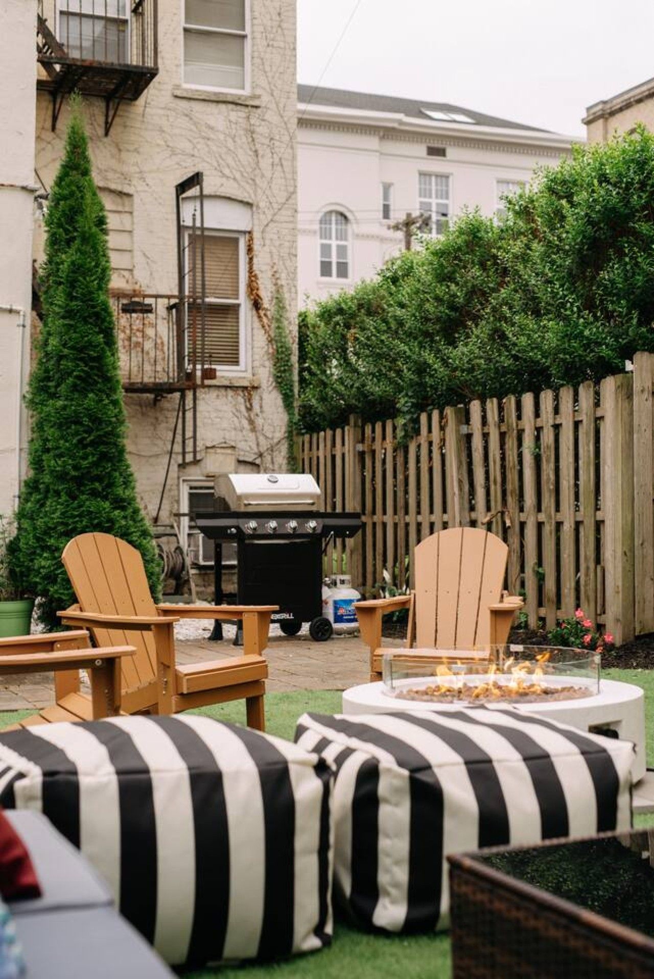 A backyard with two Adirondack chairs, a fire pit, and a grill.