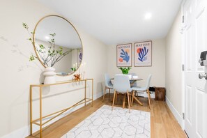 A modern interior with a round mirror, a console table, a dining area with chairs, and two framed artworks on the wall. - Chic Luxe mins NYC & MetLife W/ Private Backyard (Hoboken)