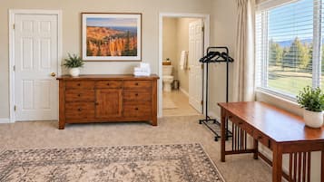 Une pièce avec une commode en bois, un tapis, une photographie de paysage encadrée et une fenêtre donnant sur un beau paysage.