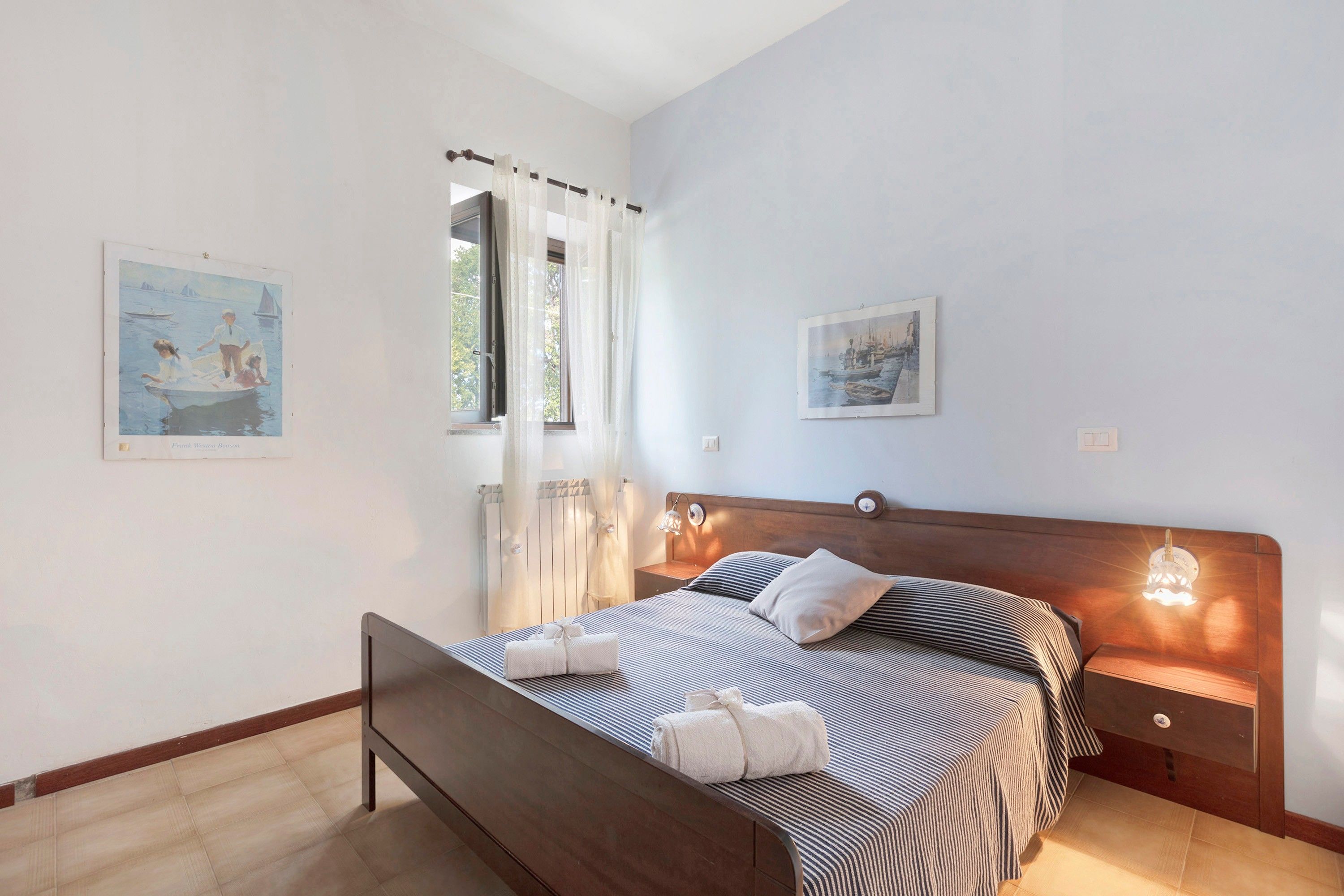 A bedroom with a bed, bedside tables, a headboard, and artwork on the walls.