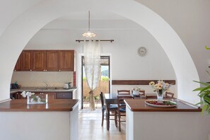 A kitchen with an arched doorway, wooden cabinets, a sink, a dining table with chairs, and a clock on the wall. - Villa "Casale del Belvedere" with sea view, private pool and Wi-Fi (San Giovanni a Piro)
