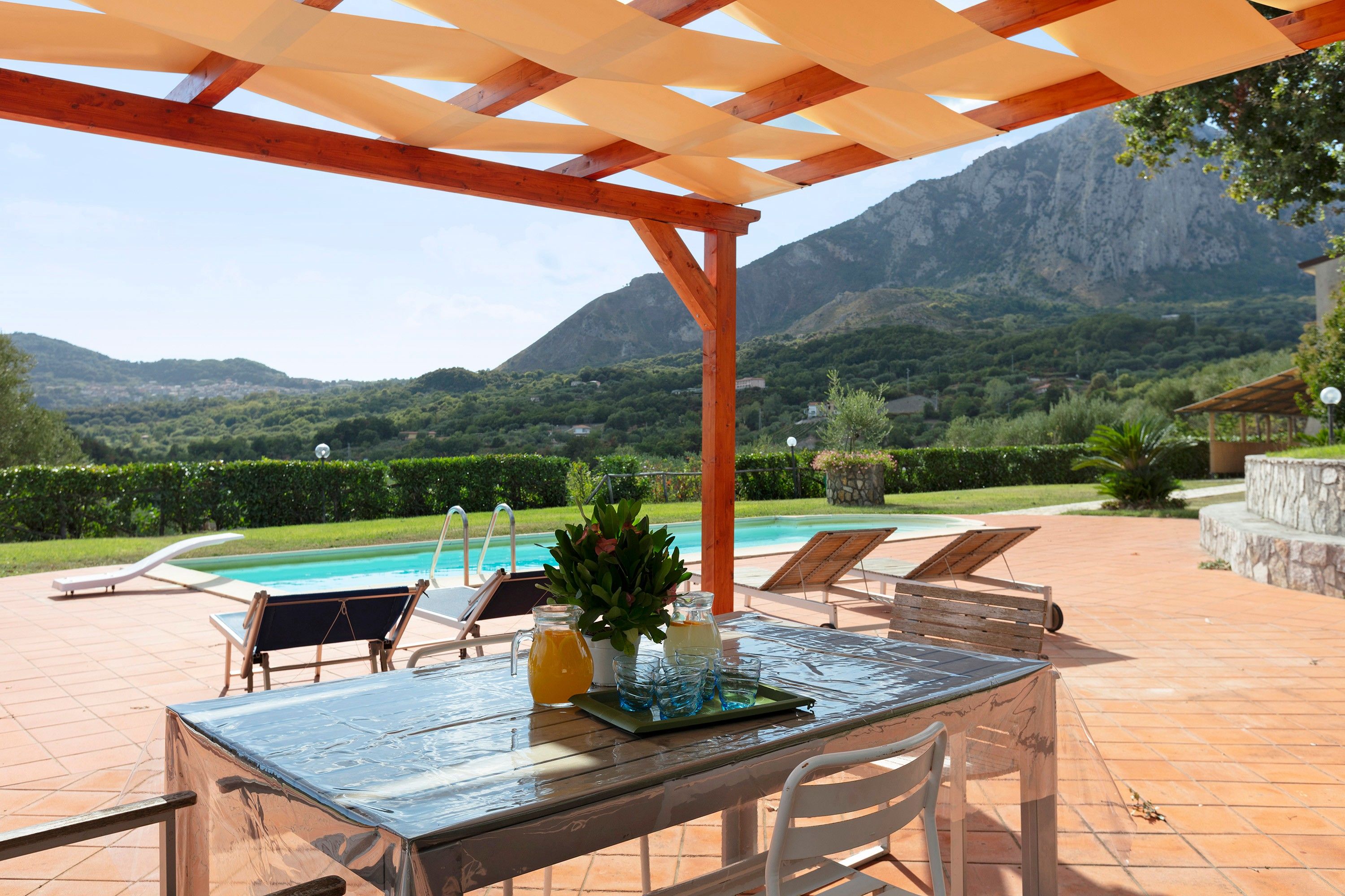 Un patio exterior con mesa, sillas y vistas a la montaña y la piscina.