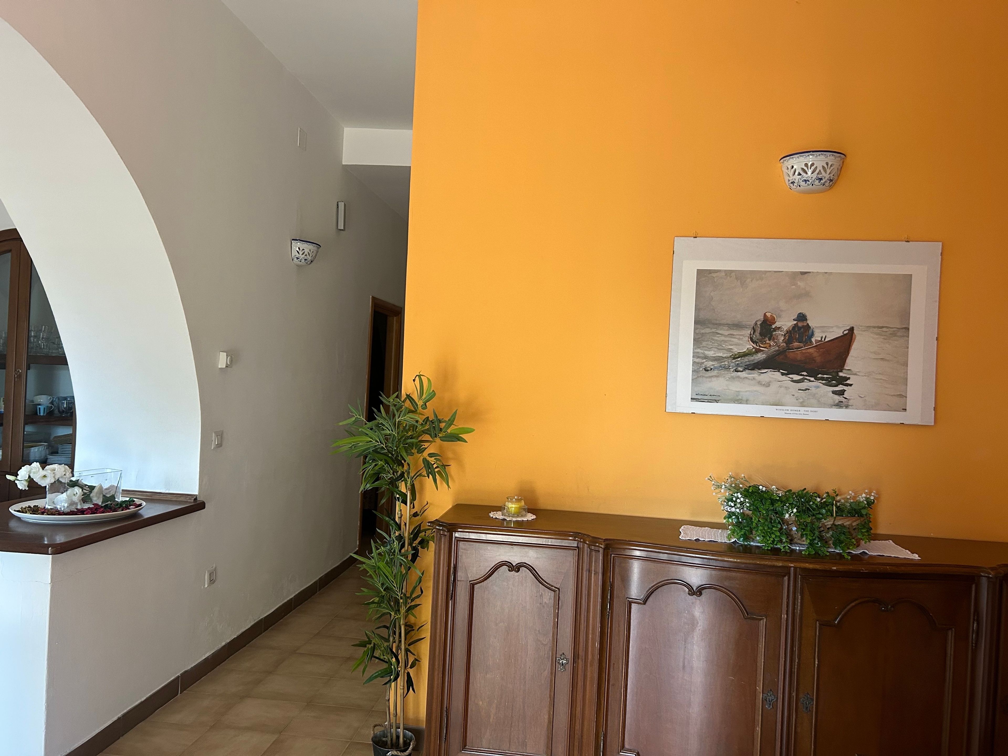 A hallway with a wooden cabinet, a potted plant, and a framed picture on the wall.