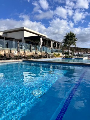 Una piscina con lettini e ombrelloni, un edificio dal design moderno e un cielo sereno.