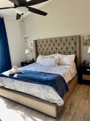 Ein Hotelzimmer mit einem großen Bett, einem Deckenventilator, Kunstwerken an den Wänden und einem Nachttisch mit einer Lampe.