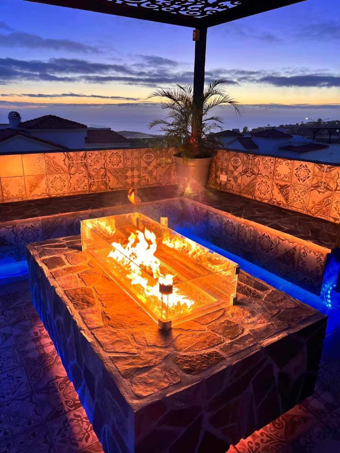 An outdoor seating area with a fire feature, patterned walls, and a view of the sky.