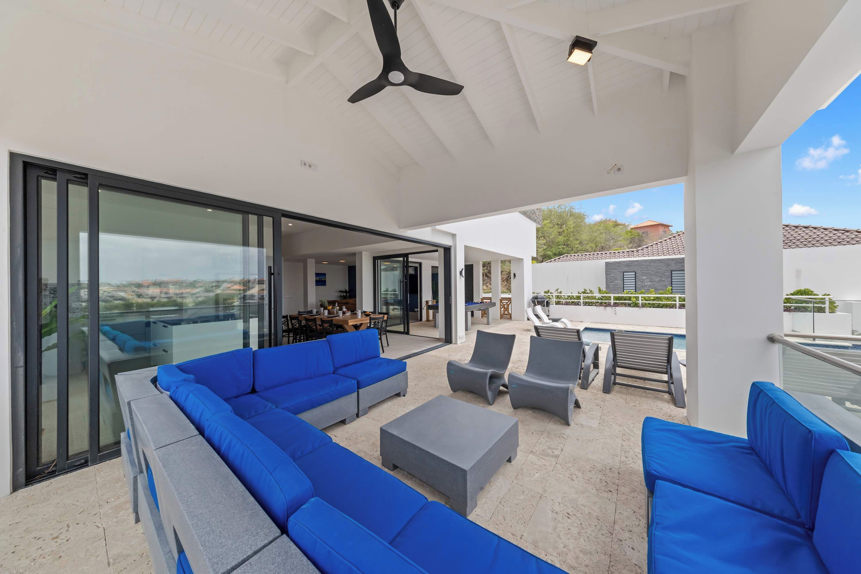 Une terrasse extérieure aménagée avec un canapé d’angle, des fauteuils et un espace piscine.