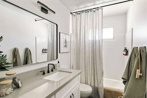 A modern bathroom with a large mirror, a sink, a toilet, and a shower curtain.