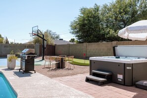 A backyard with a pool, a hot tub, a barbecue grill, and outdoor seating.