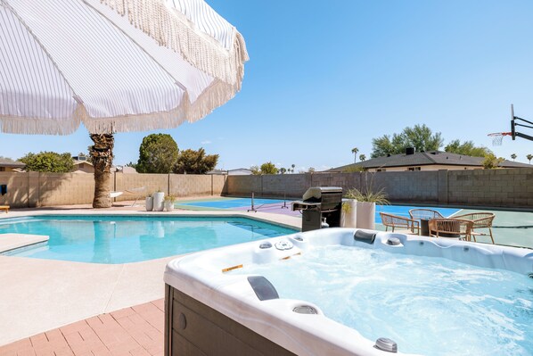 A swimming pool with a hot tub, lounge chairs, and an umbrella.