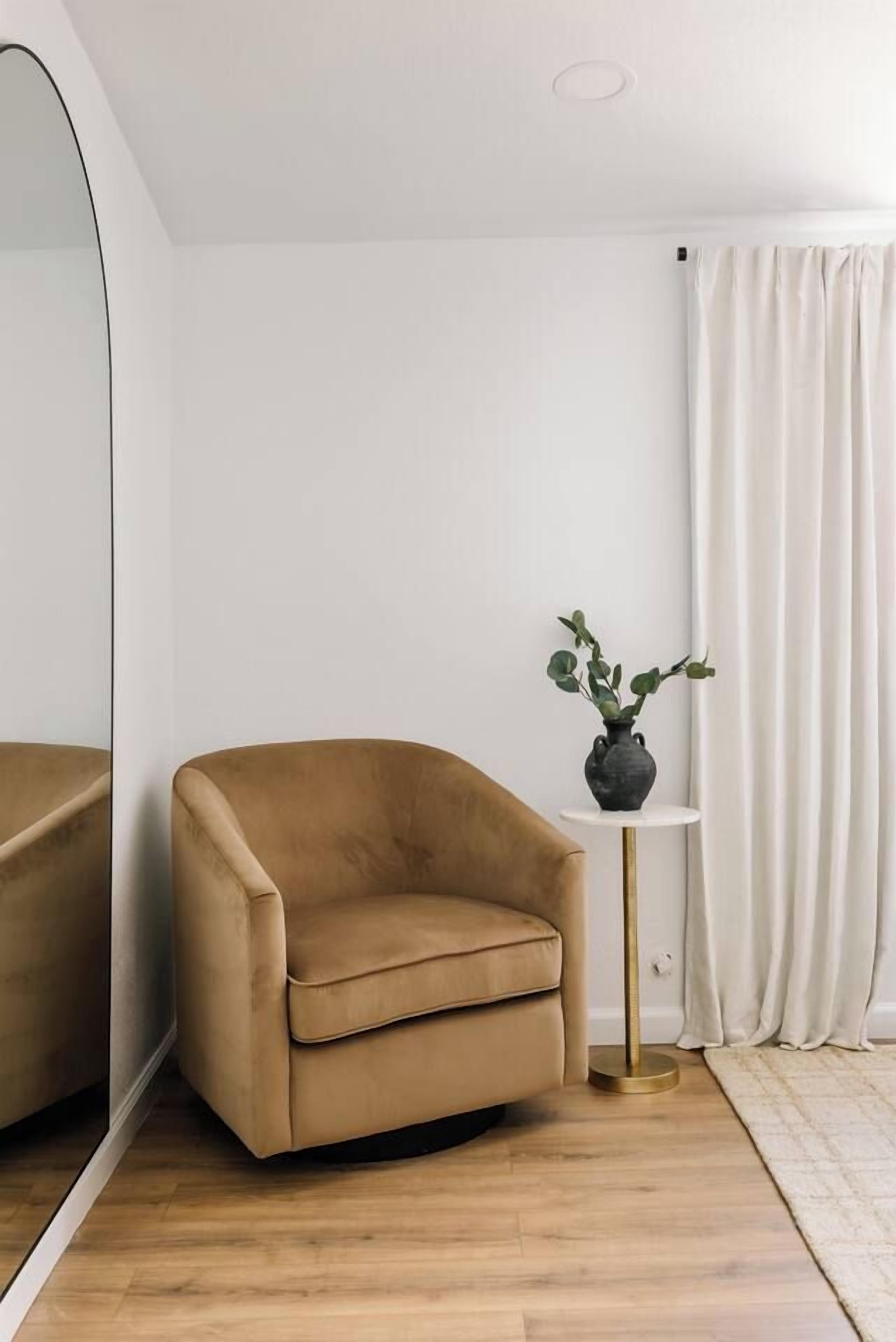 A room with a brown armchair, a small round table with a plant, and a white curtain.
