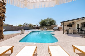 A swimming pool with lounge chairs, a barbecue area, and a covered patio with outdoor furniture.