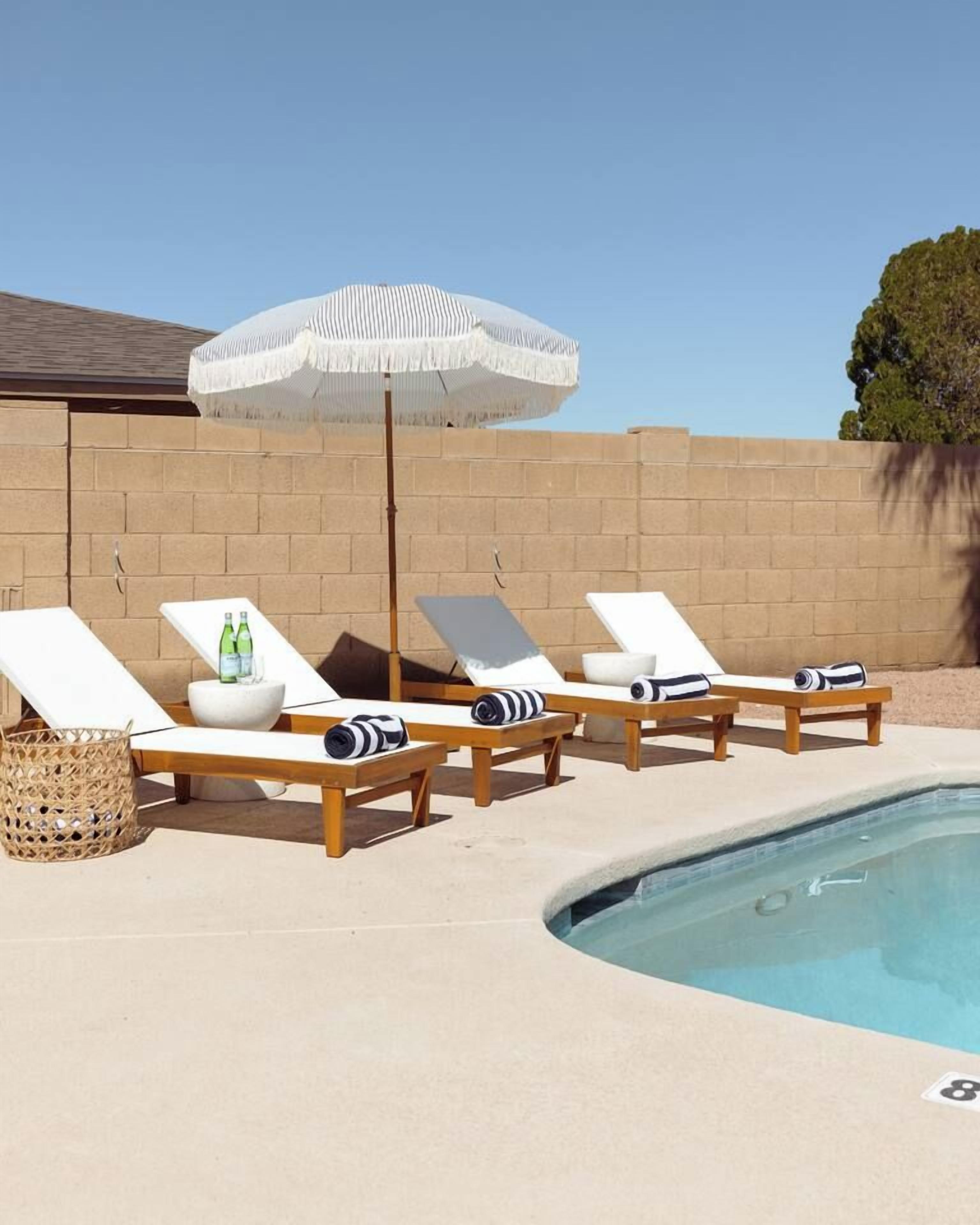 A poolside area with lounge chairs, a white umbrella, and a small table with bottles.