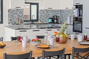 Eine moderne Küche mit Essbereich, ausgestattet mit einer Granitarbeitsplatte, Edelstahlgeräten und einer Auswahl an Obst und Getränken auf dem Tisch.