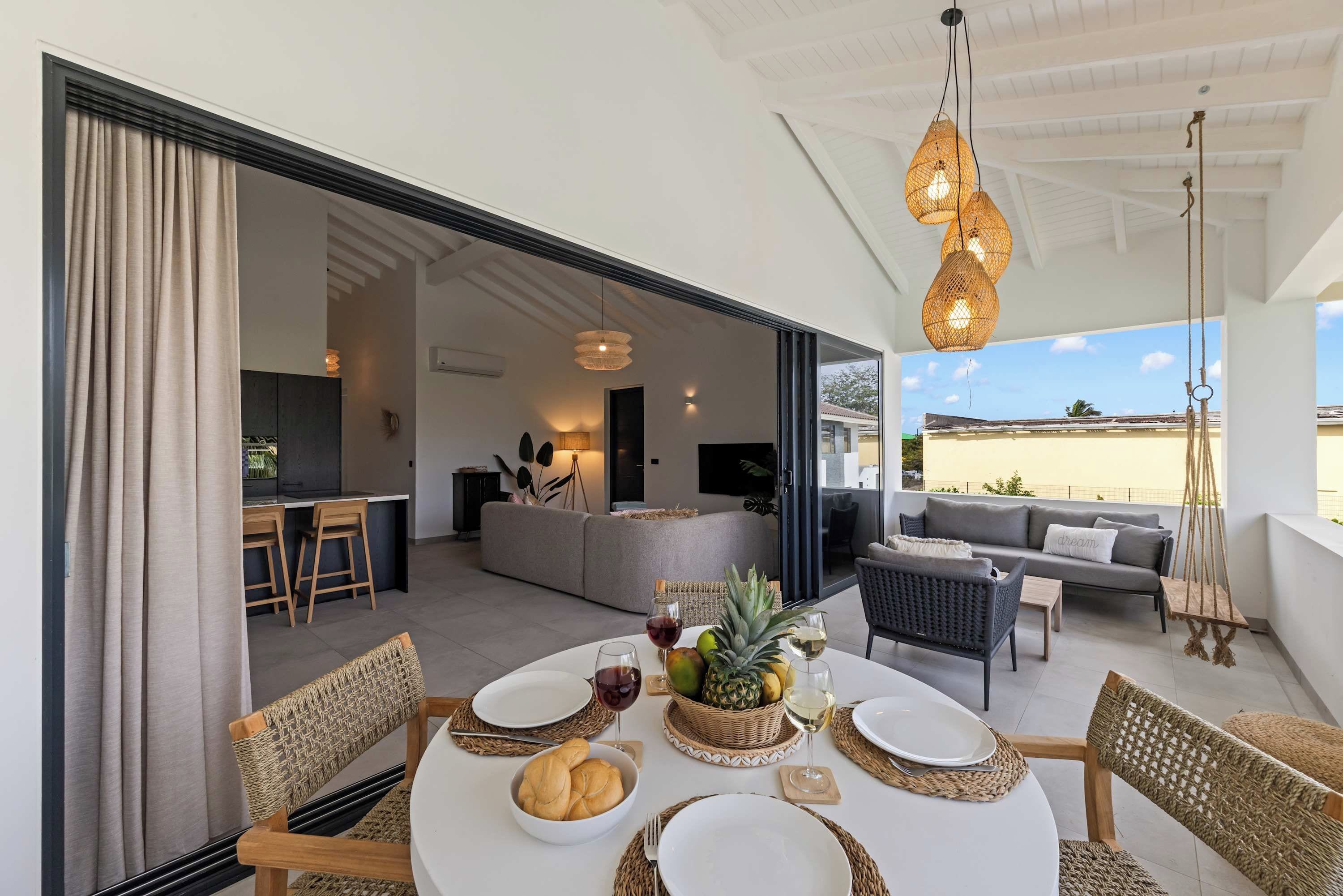 Un espacio habitable de concepto abierto con una mesa de comedor para dos personas, una cocina al fondo y un balcón con mobiliario exterior.