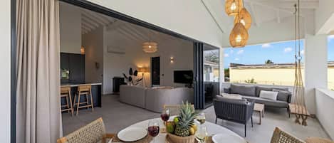 Un espacio habitable de concepto abierto con una mesa de comedor para dos personas, una cocina al fondo y un balcón con mobiliario exterior.