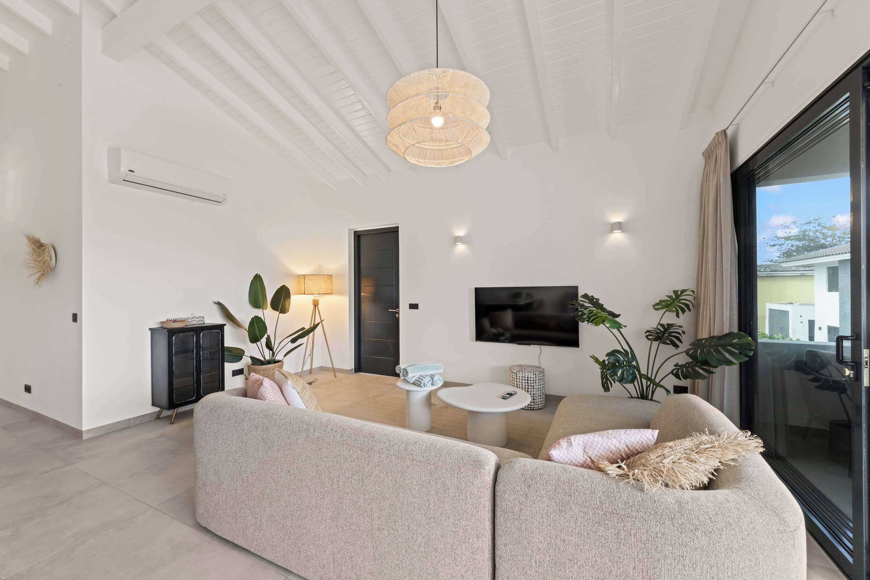 A modern living room with a large sectional sofa, a round coffee table, and a flat-screen TV mounted on the wall.